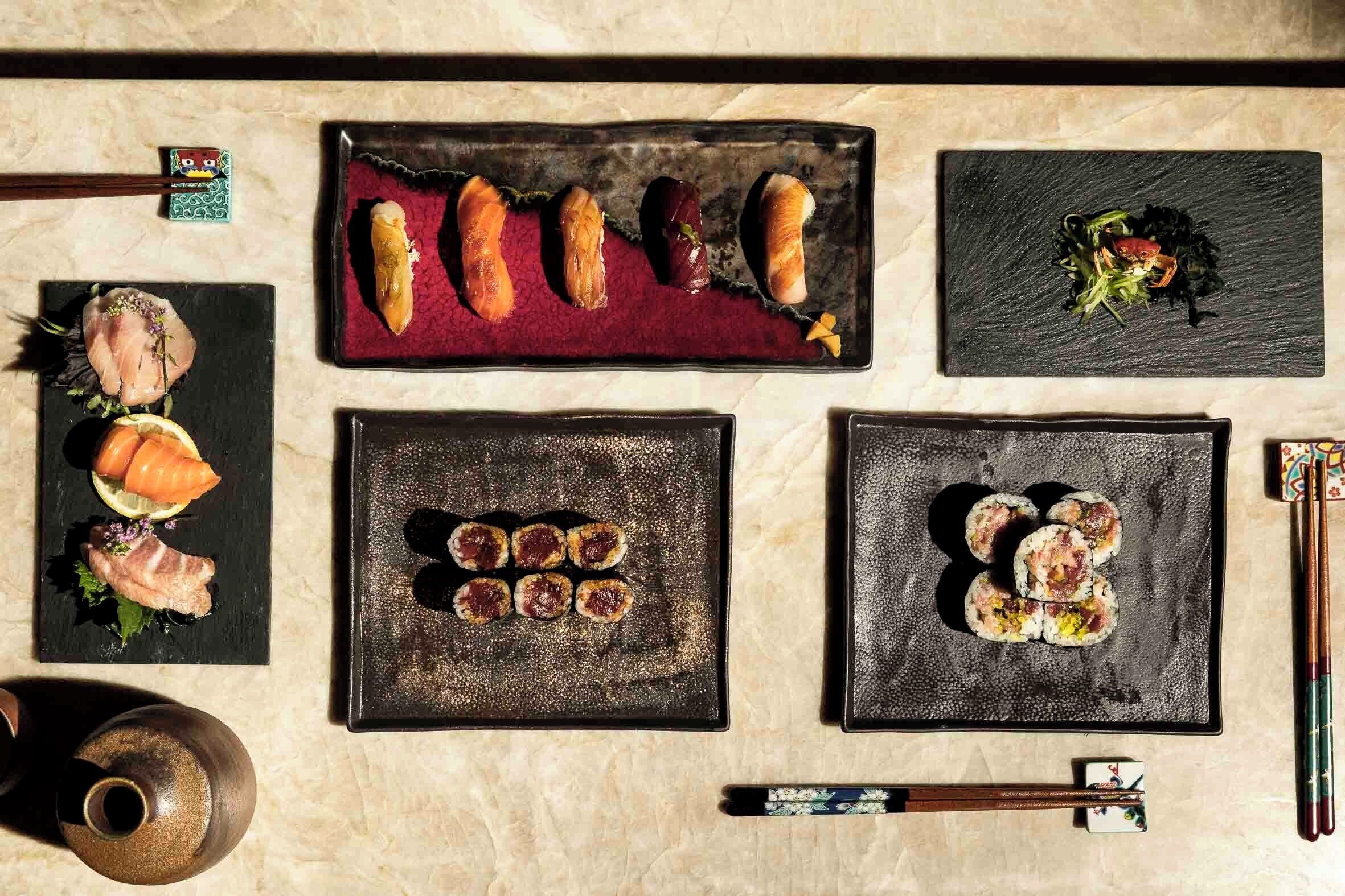A variety of sushi dishes arranged on black plates, with chopsticks and a small decorative item on the table.