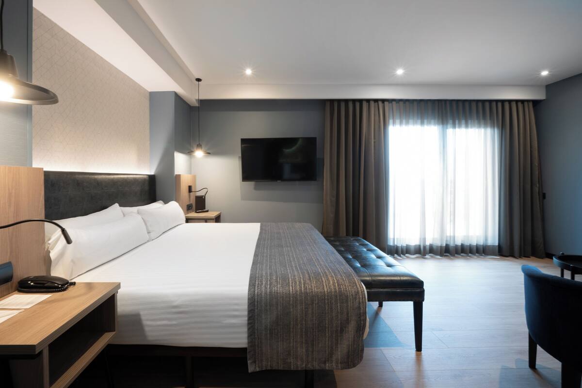Ein modernes Hotelzimmer mit einem großen Bett, einer Bank, einem Schreibtisch und einem Fernseher.