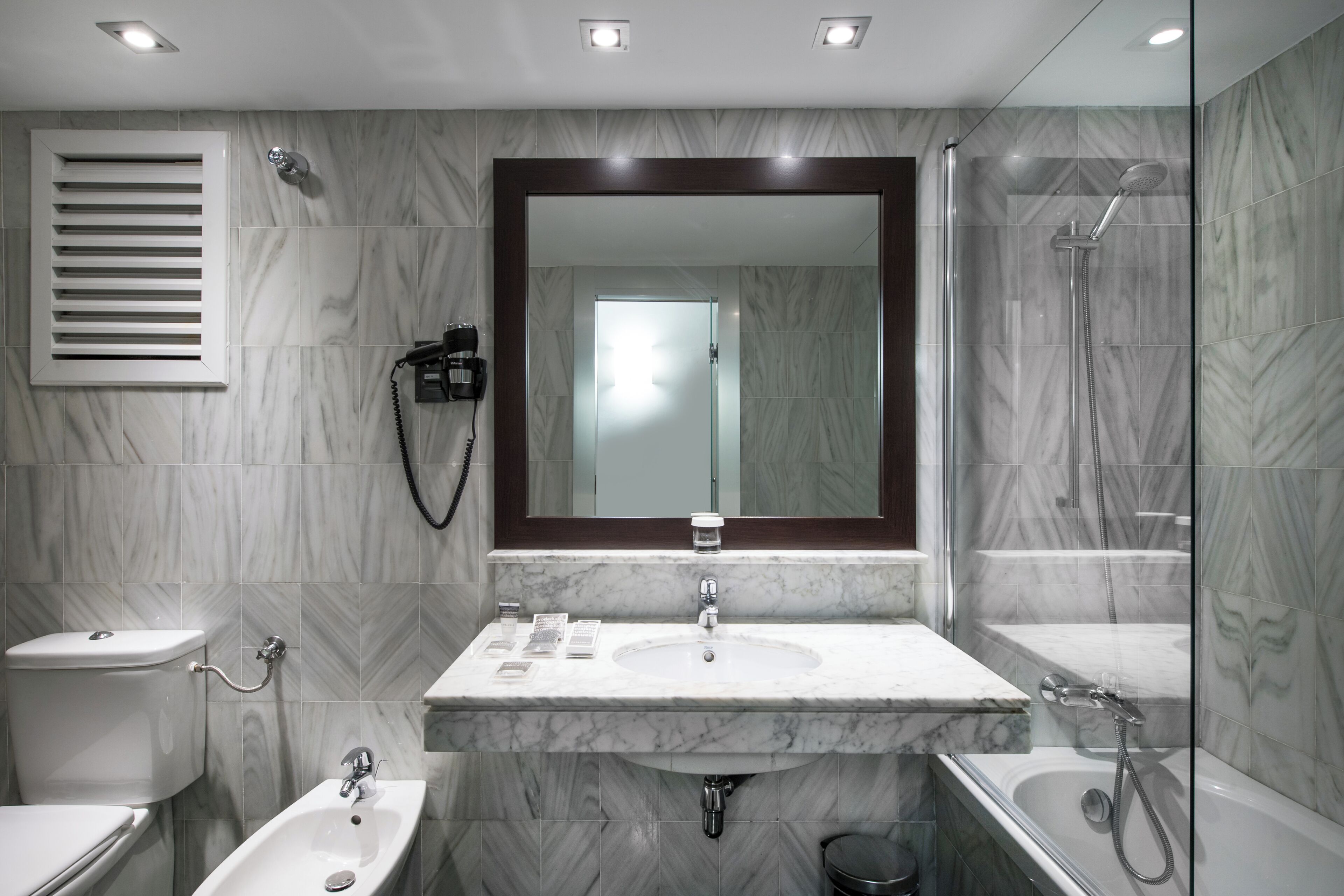 A modern bathroom with a marble sink, a toilet, a bathtub, and a shower.
