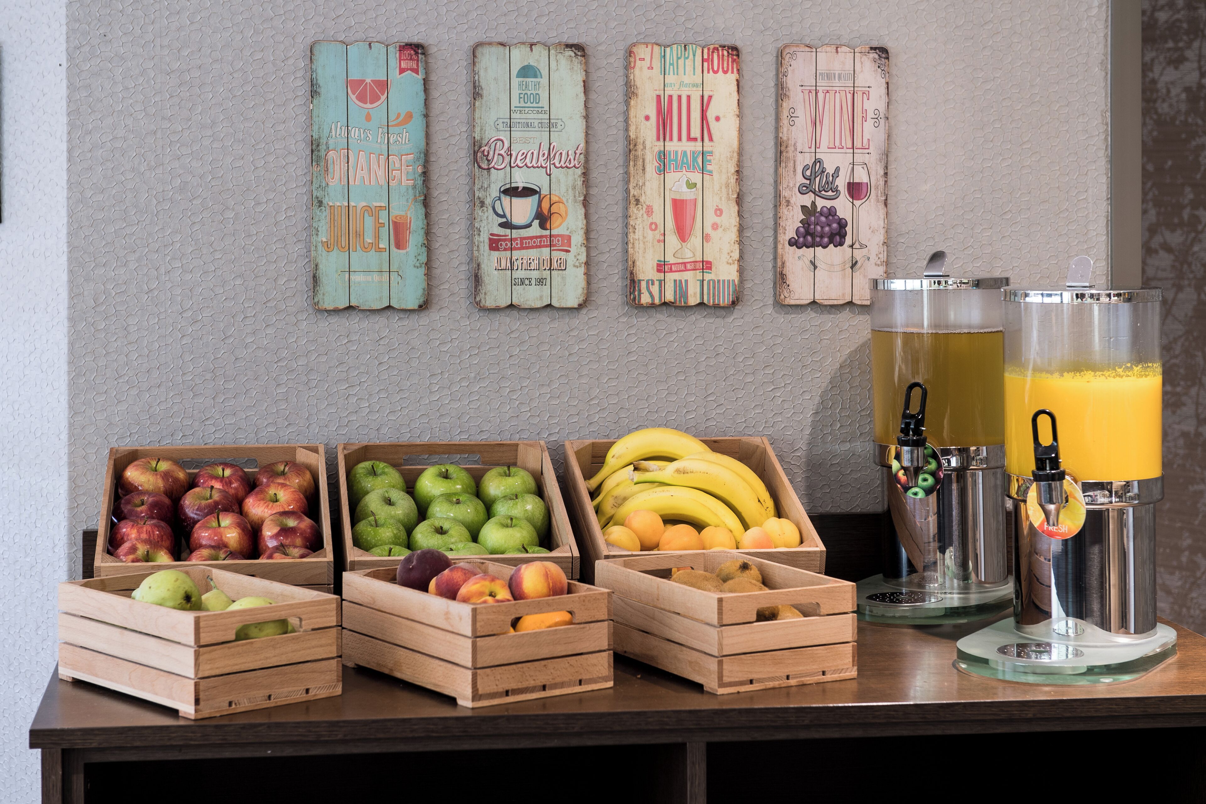 Un bar où l’on prend le petit-déjeuner, avec des caisses en bois remplies de fruits, une enseigne publicitaire pour des milkshakes et une machine à café.