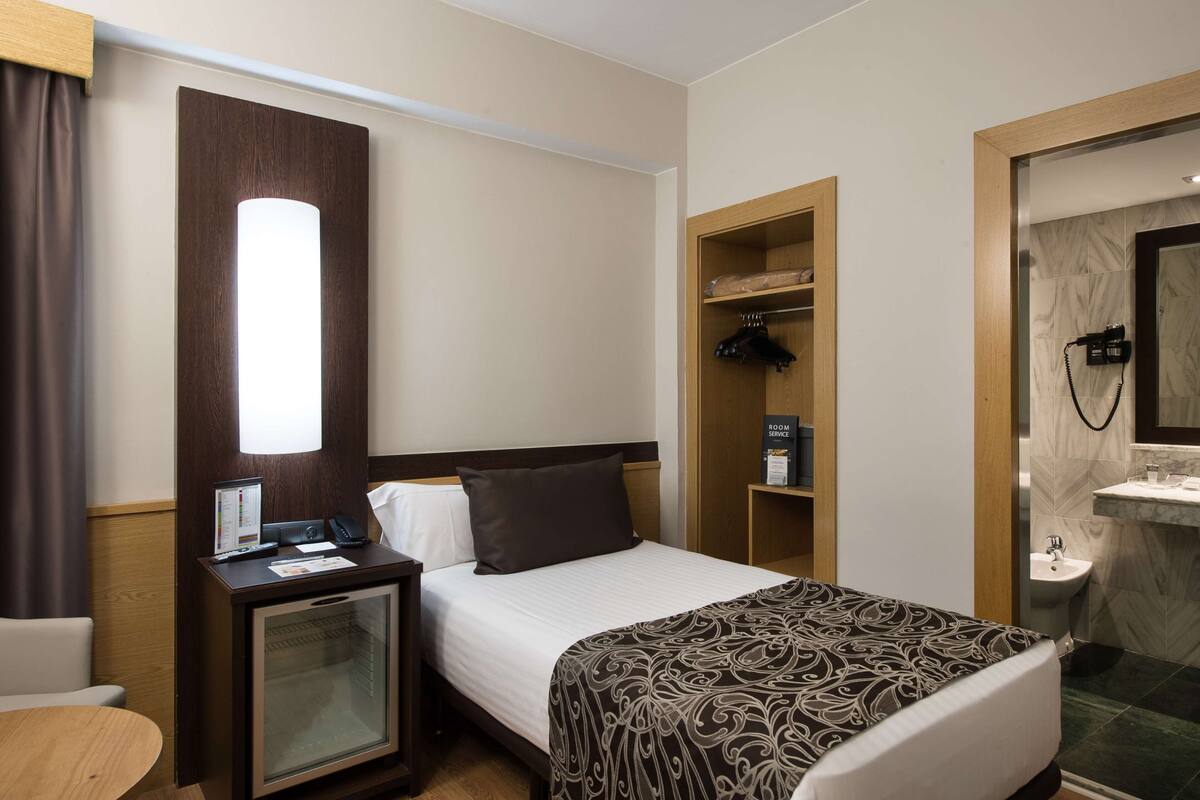 Ein Hotelzimmer mit Bett, Nachttisch, Schreibtisch und einem Badezimmer mit Waschbecken und Spiegel.