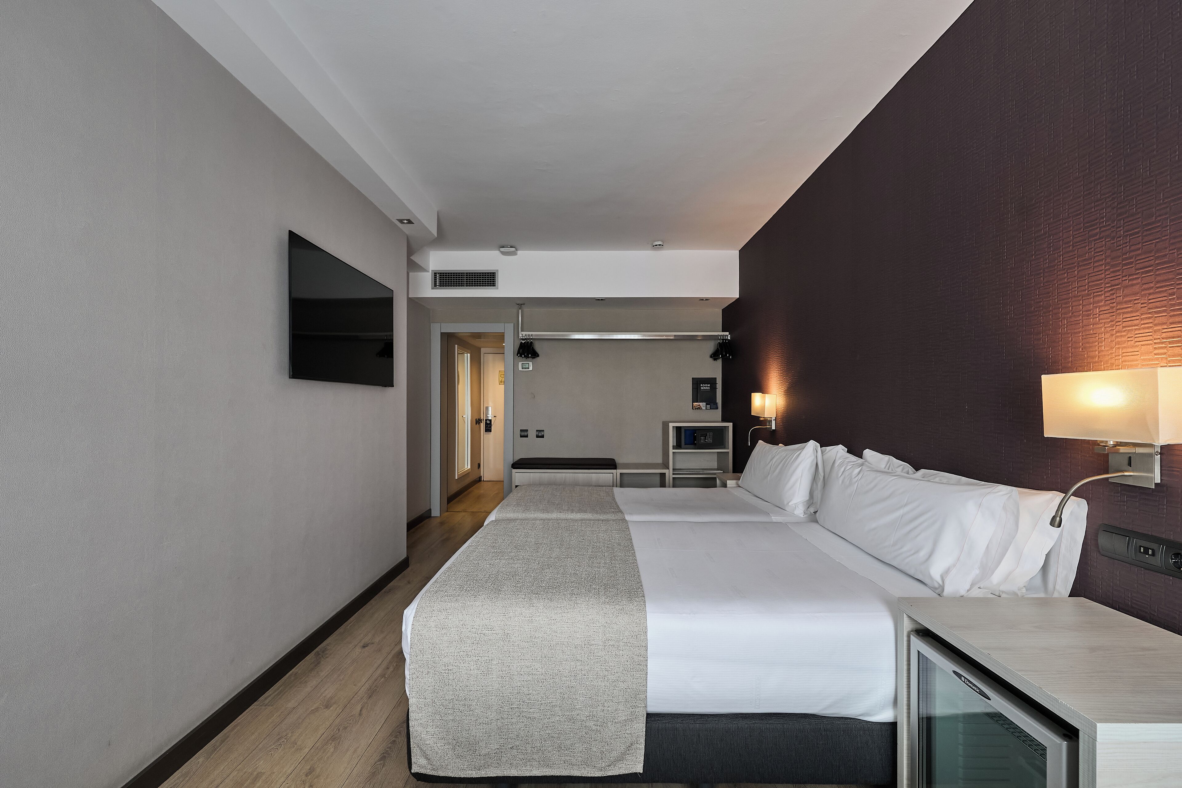 Une chambre d’hôtel avec un grand lit, des tables de chevet, un téléviseur à écran plat et une lampe fixée au mur.