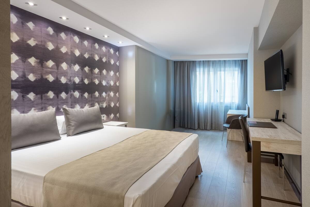 Ein Hotelzimmer mit Bett, Schreibtisch, Fernseher und einem Fenster mit Vorhängen.