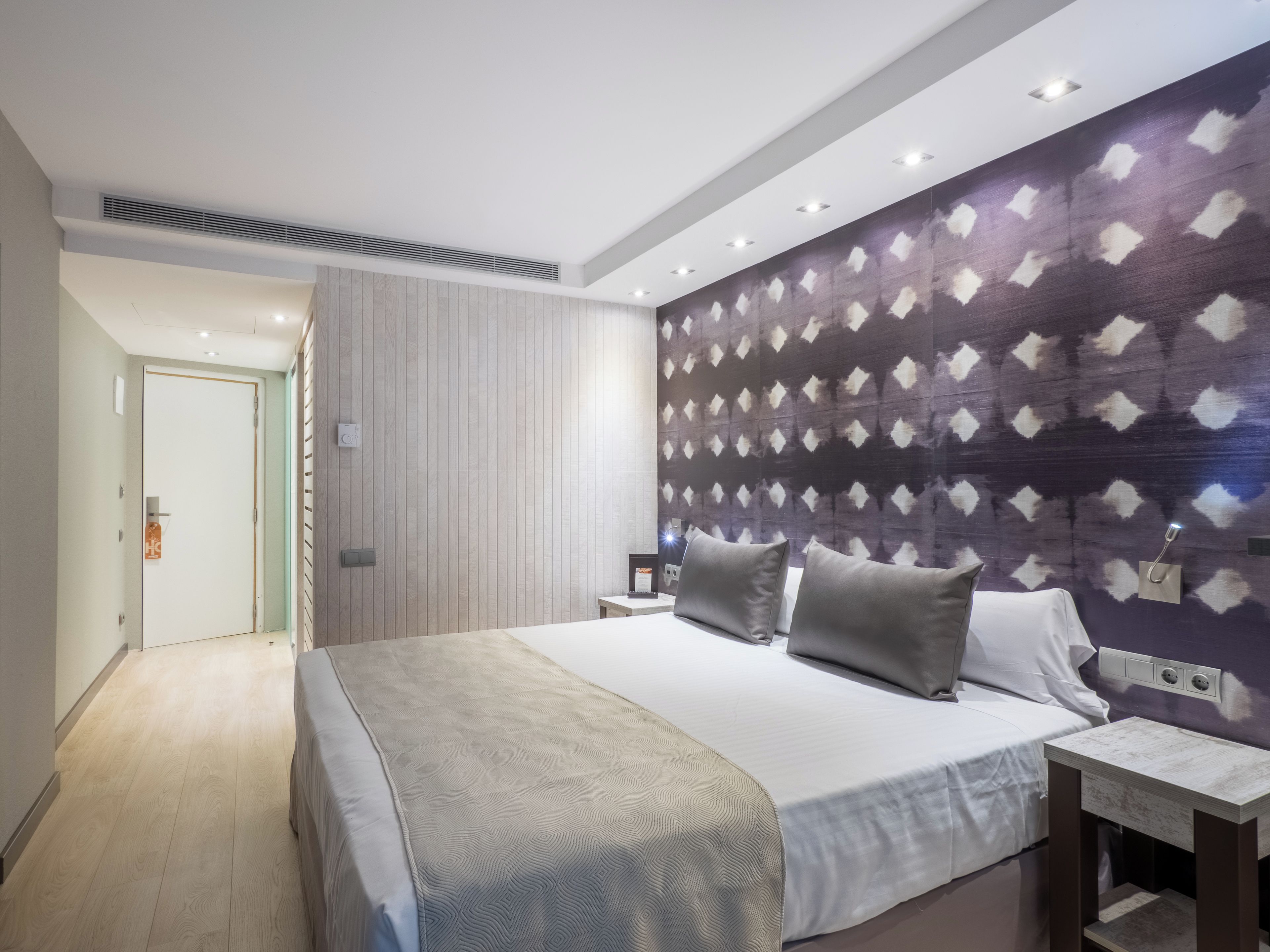 Een moderne hotelkamer met een groot bed, nachtkastjes en een behang met een patroon.