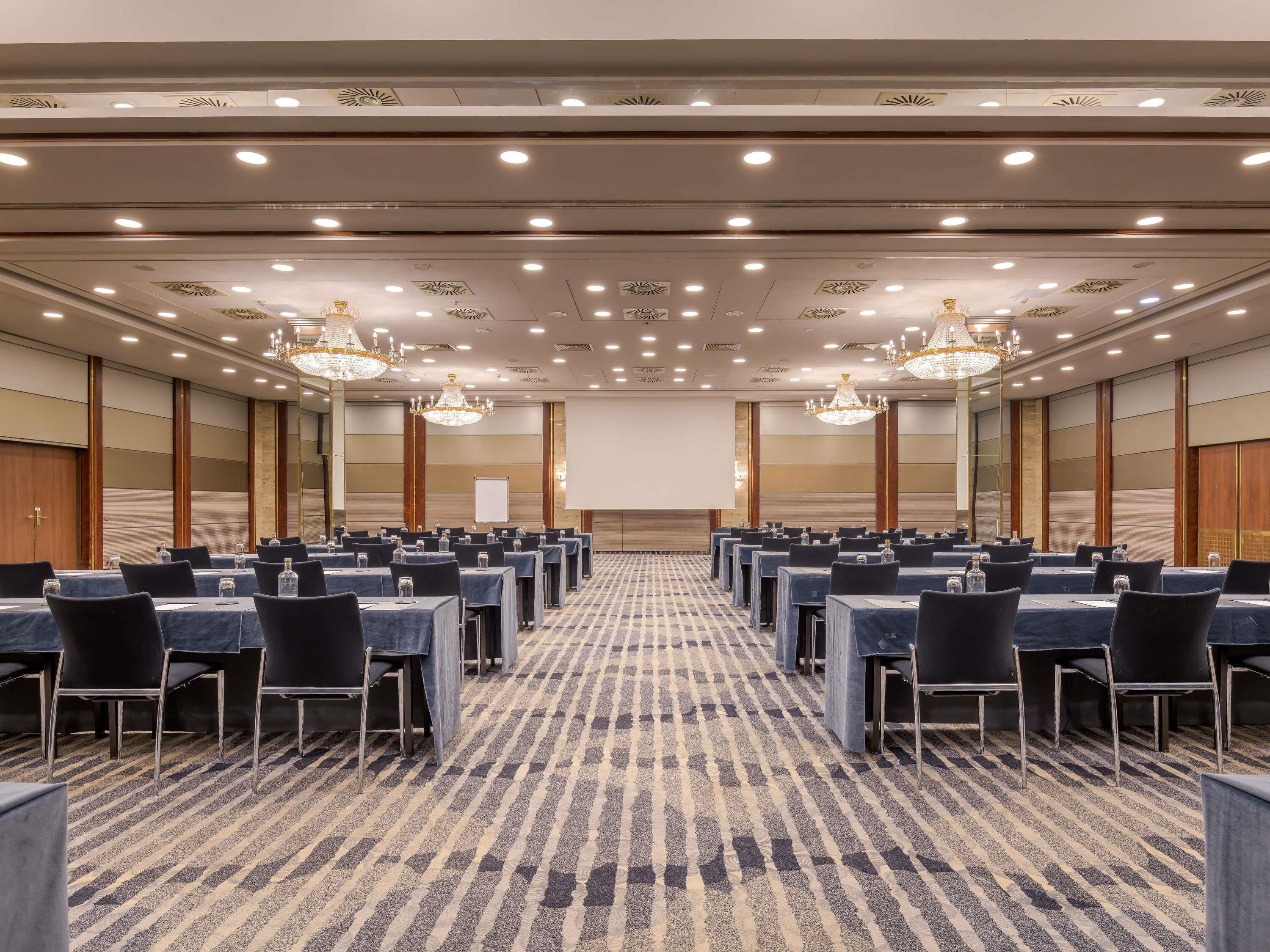 A conference room with rows of tables, chairs, and chandeliers.