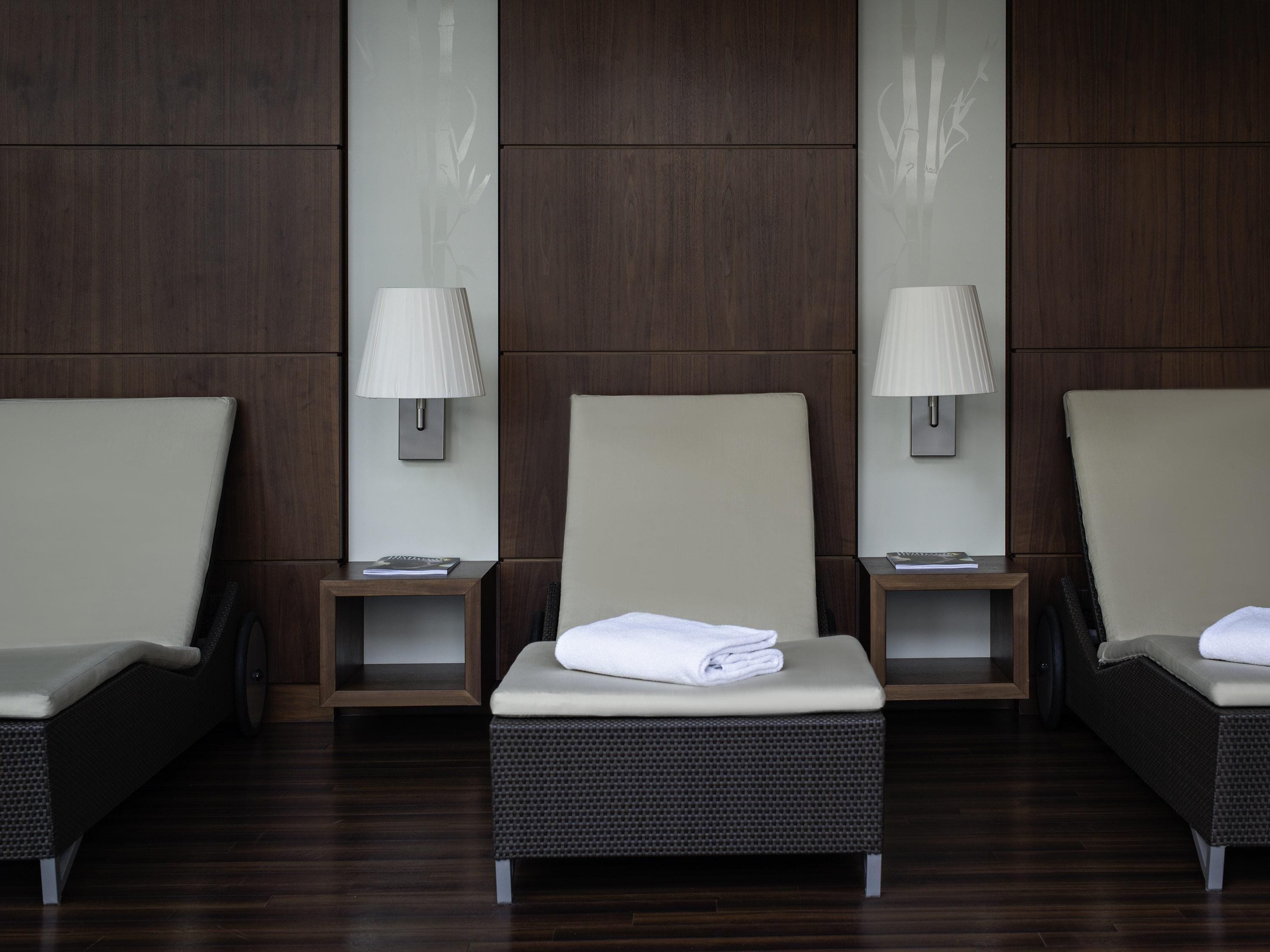 A hotel room with three reclining chairs, each with a side table and a lamp.