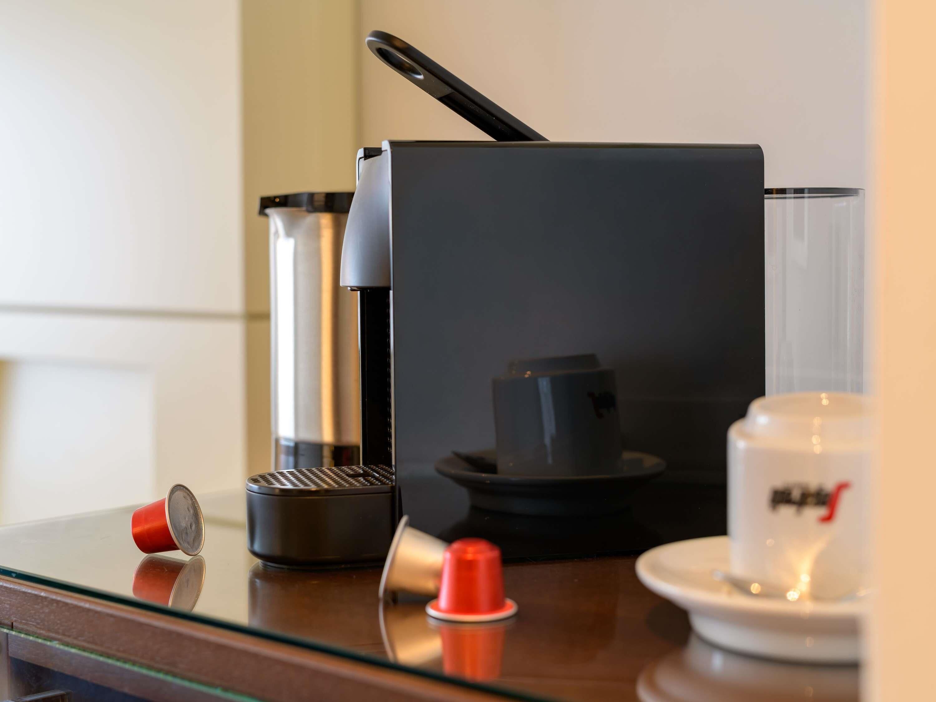 En kaffemaskine, et glas og en hvid kop på et glastilbord.