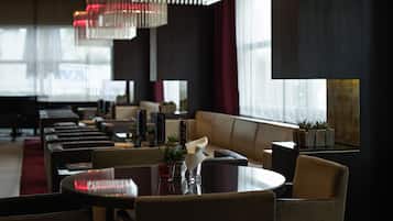 A modern dining area with round tables and cushioned seating, large windows with curtains, and decorative red lighting.