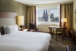 A hotel room with a large bed, a desk, a chair, and a view of a cityscape.