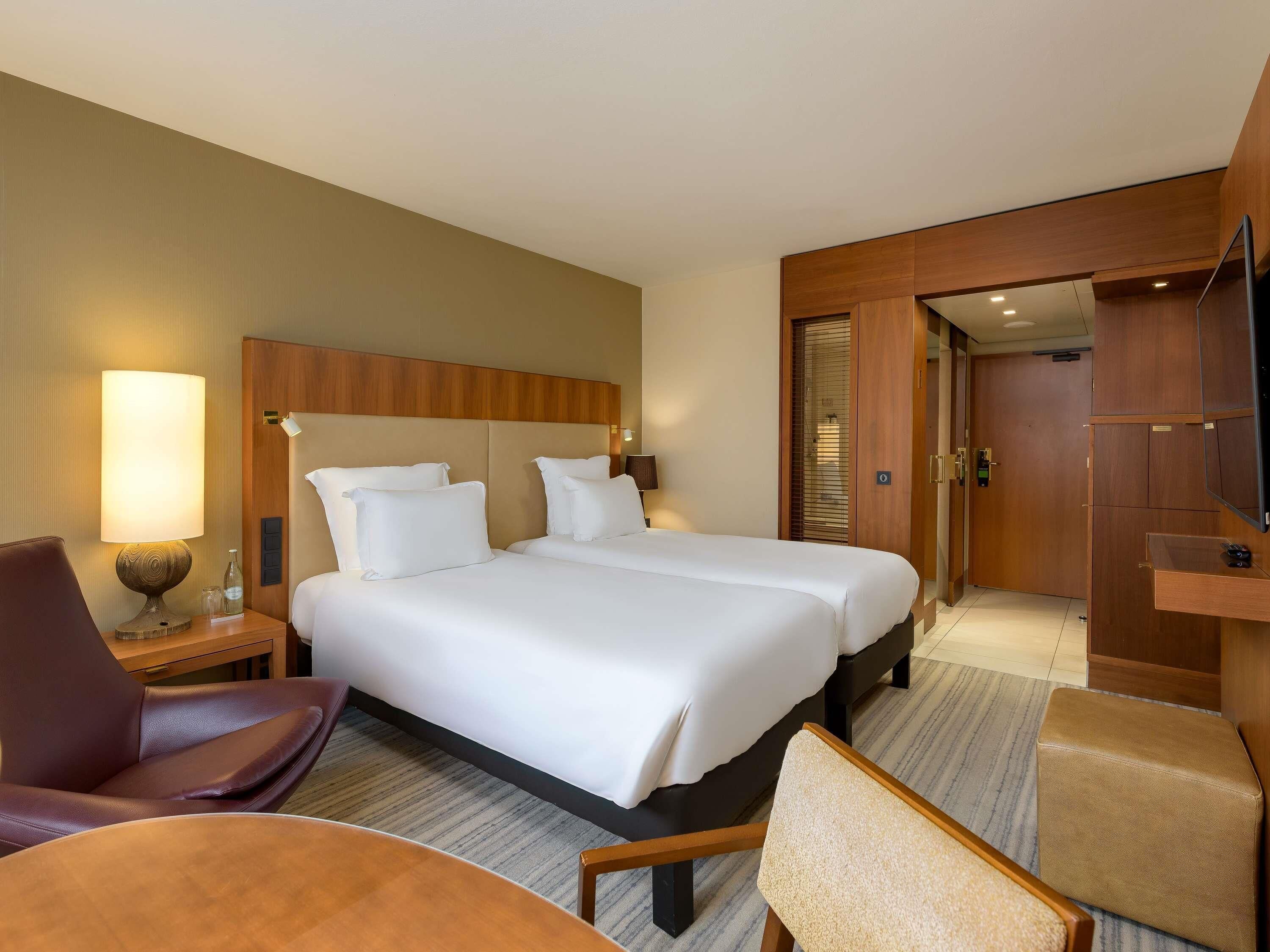 A hotel room with a large bed, a desk, a chair, and a TV.