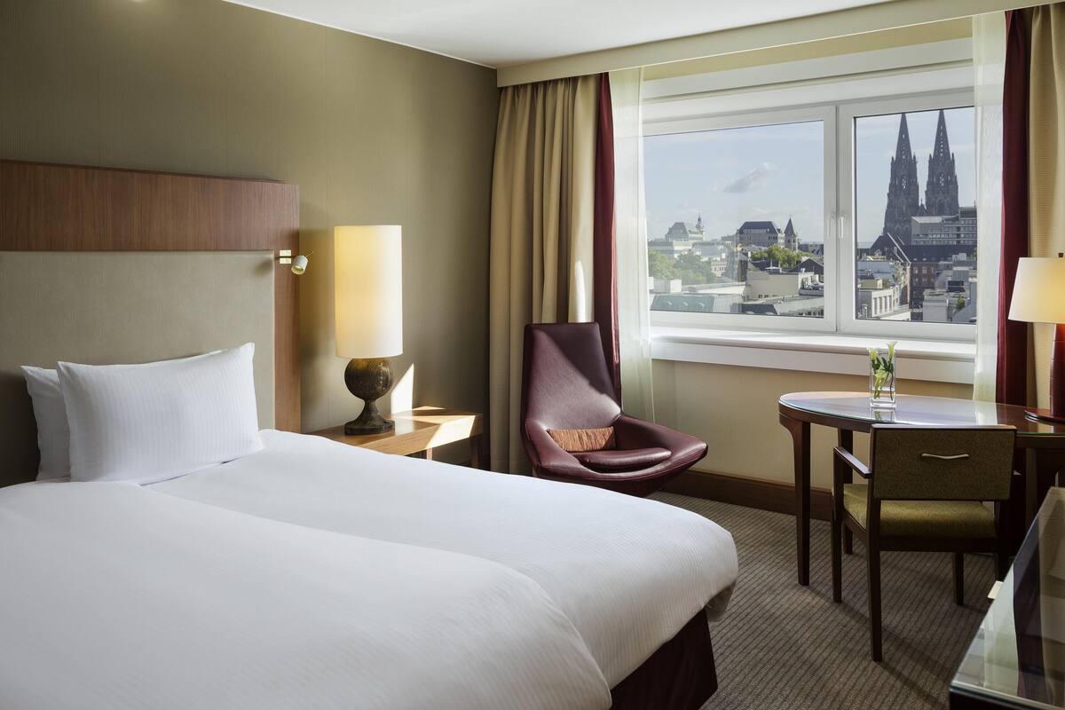 Une chambre d’hôtel avec un grand lit, une chaise, une petite table et une fenêtre donnant sur la ville.