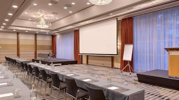 Un salón de conferencias con un escenario, una pantalla de proyector y un atril.