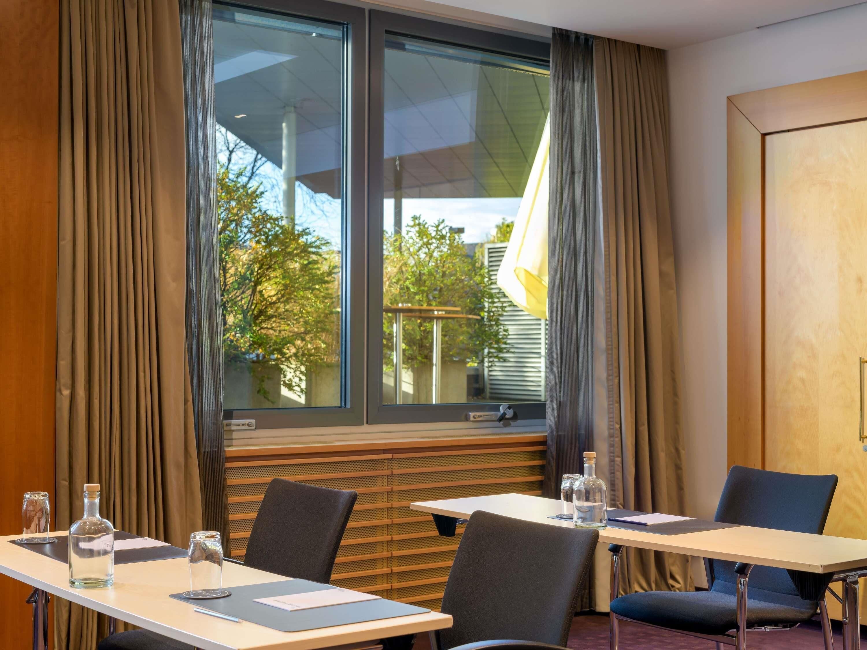 A hotel room with a large window, a table with chairs, a bottle, and a glass.