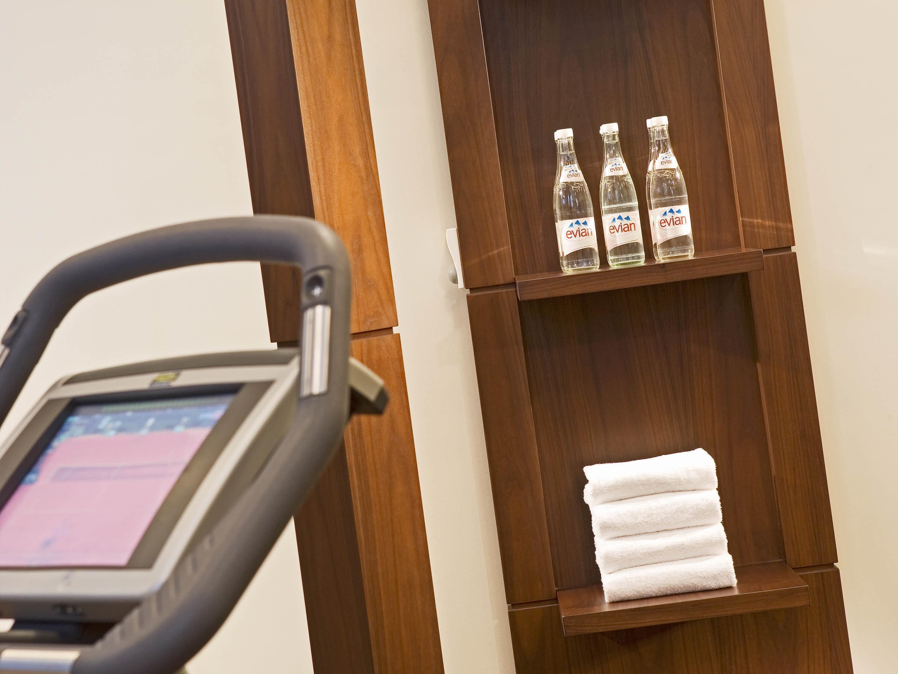 Baño con repisa de madera que sostiene tres botellas de Evian y una pila de toallas blancas.