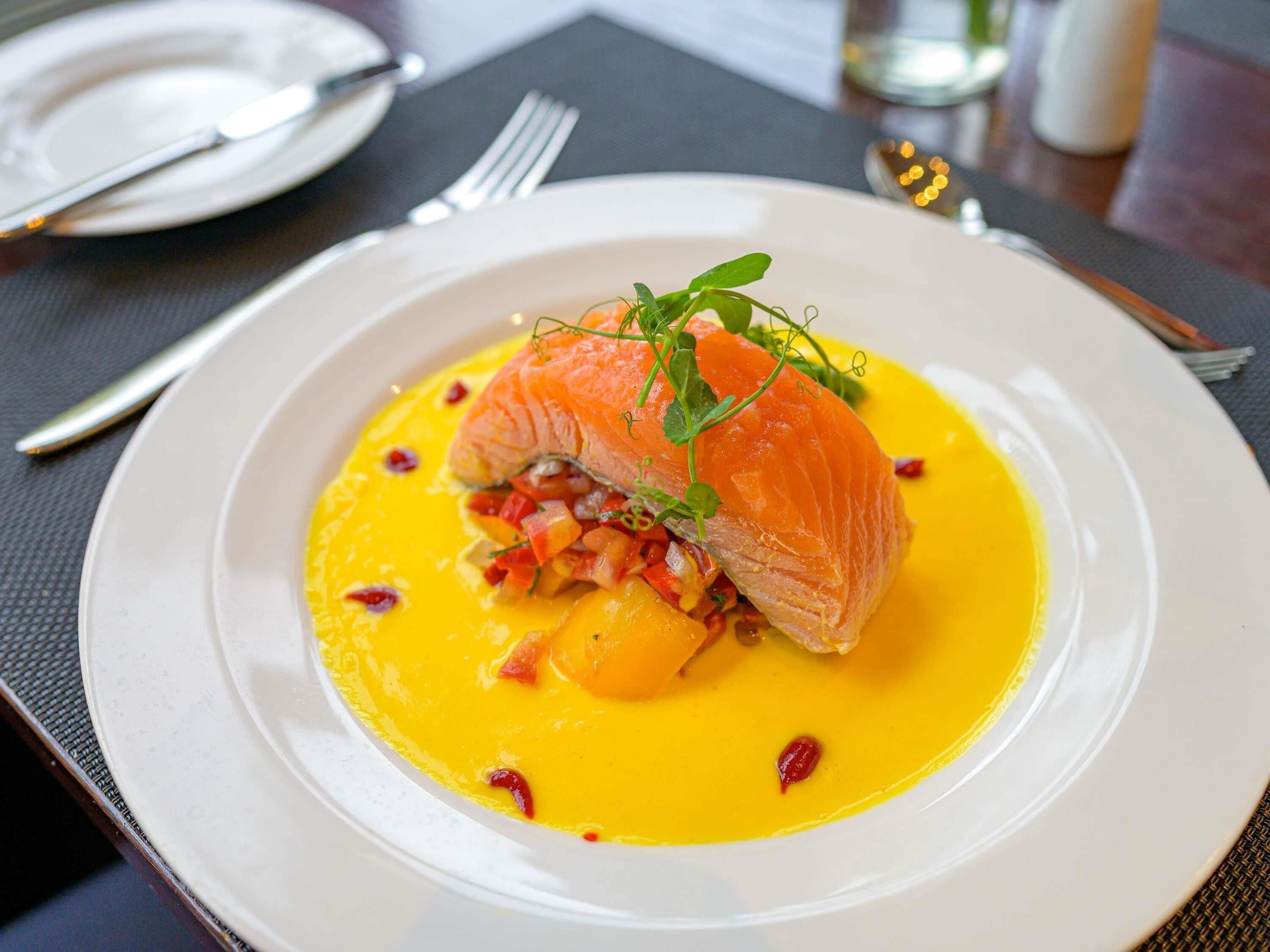 A plate of food with salmon, a yellow sauce, and garnishes.