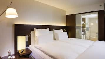 A hotel room with a bed, bedside table, lamp, and a view of the bathroom.