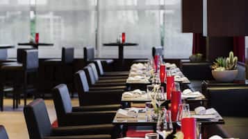 A restaurant with long tables set for dining, chairs, and a potted plant on the side.