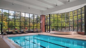 Una amplia piscina interior con paredes de vidrio transparente, rodeada de sillones de descanso y un muro de ladrillo.