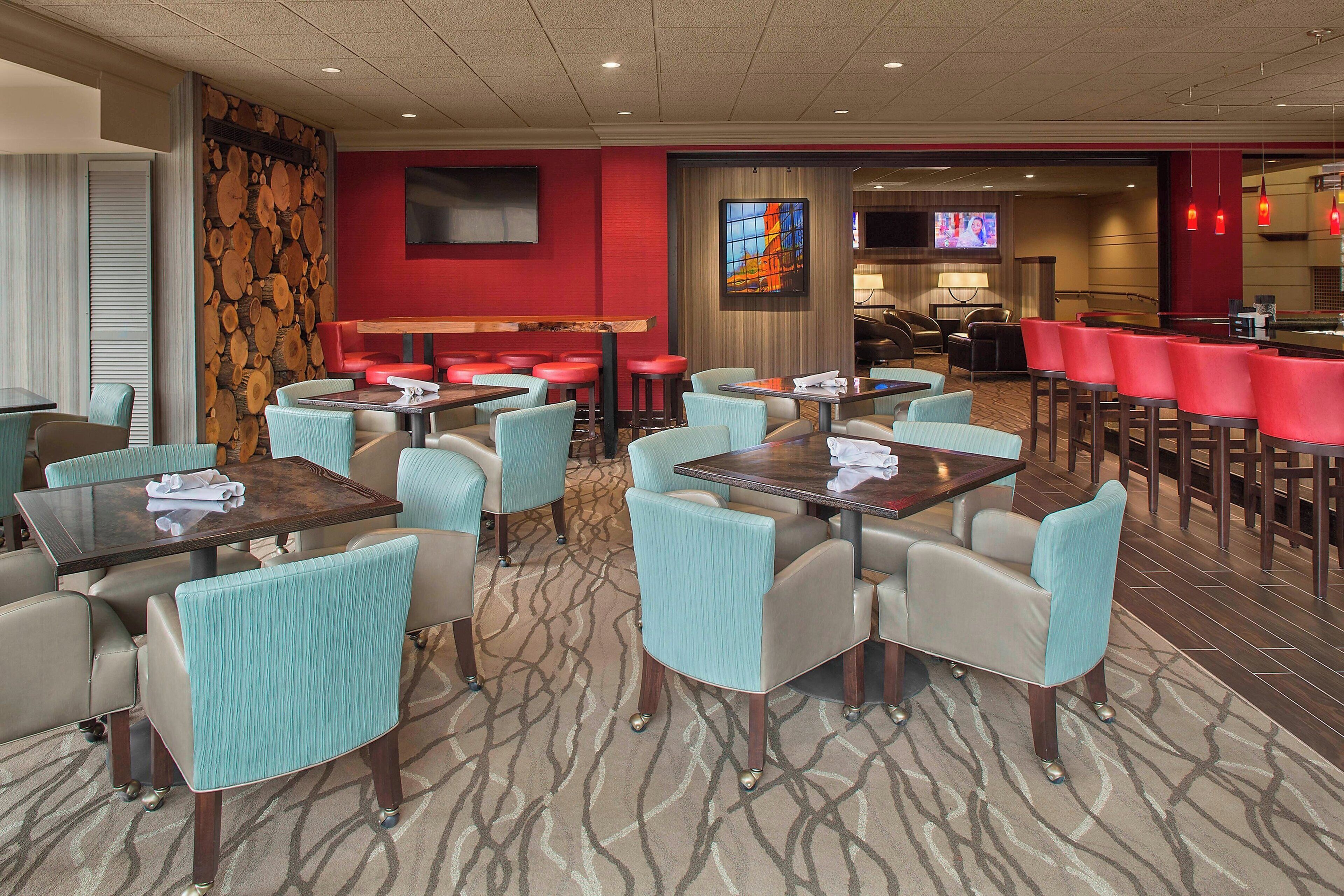 Un hall d’hôtel comprenant un bar, des espaces aménagés avec des sièges et un écran de télévision.