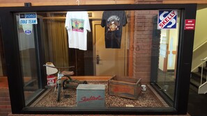 Une vitrine exposant divers objets, notamment un extincteur ancien, une caisse en bois et une enseigne sur laquelle on peut lire « Sealtest ».