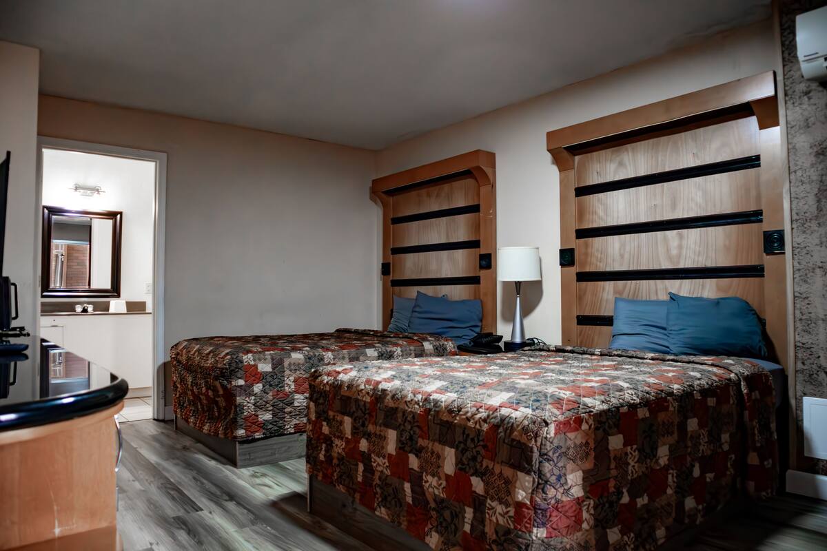 A hotel room with two beds, a desk, and a mirror.