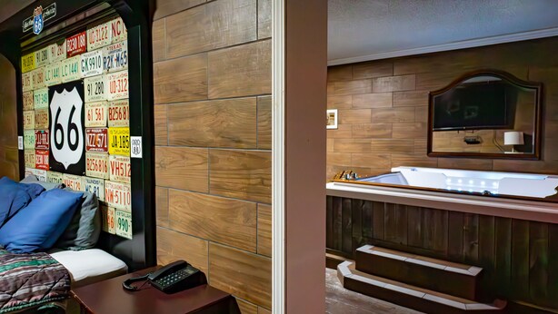 A hotel room with a wooden wall, a bed with blue pillows, a desk with a phone, and a wooden panel wall with license plates. - Route 66 Hotel, Springfield, Illinois (Springfield)