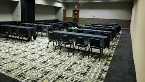 A conference room with rows of tables and chairs, a patterned carpet, chandeliers, and an exit sign. - Route 66 Hotel, Springfield, Illinois (Springfield)