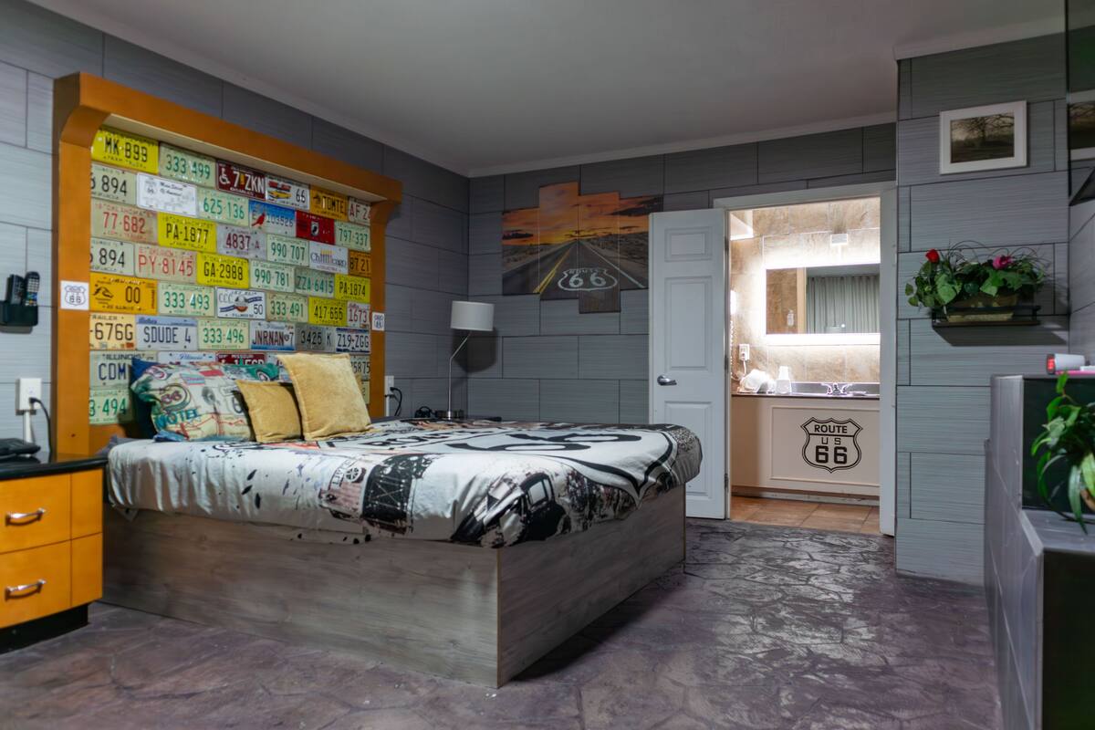 A bedroom with a bed, a dresser, a nightstand, and a wall decorated with license plates.