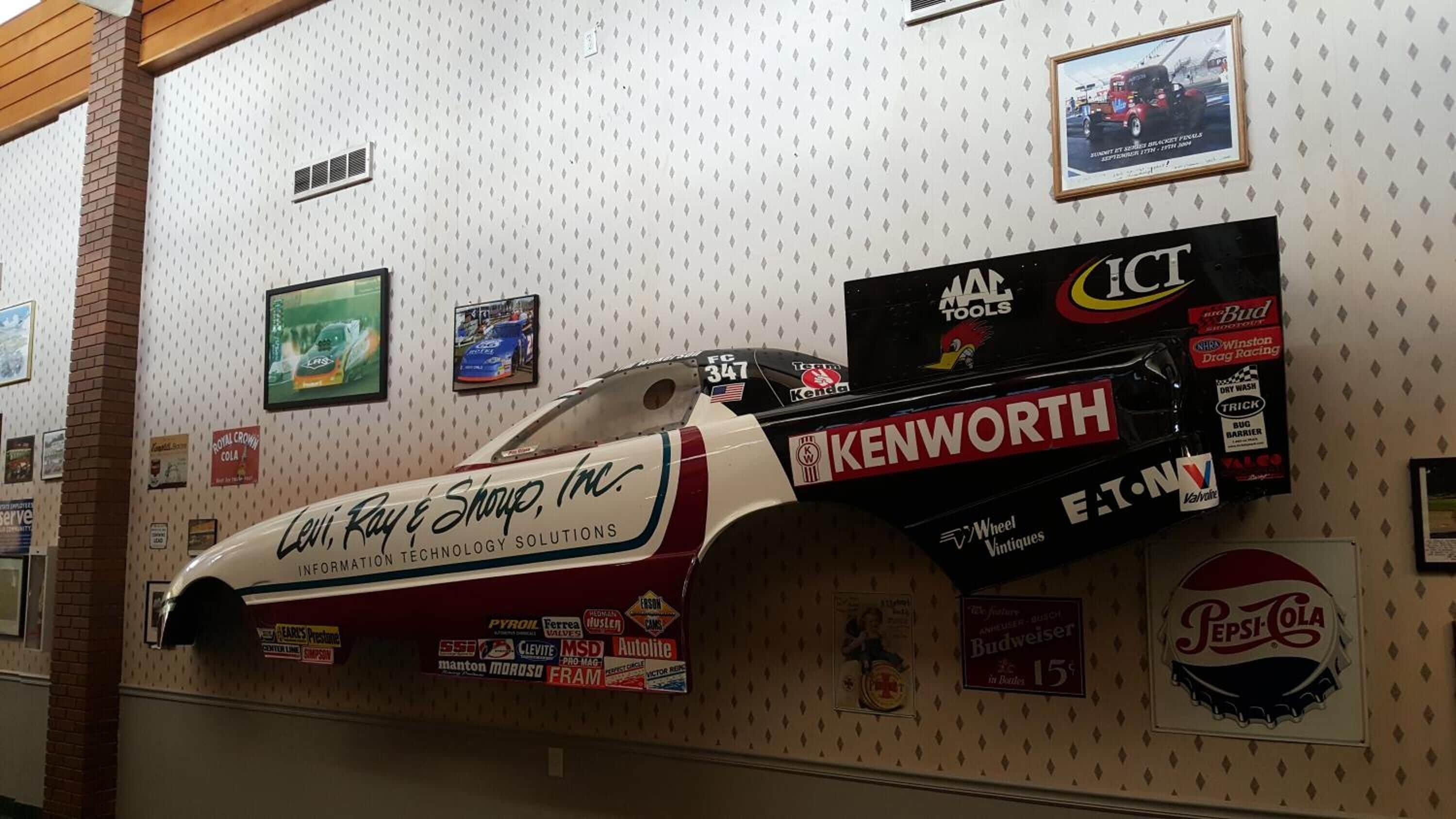 A wall with a racing car model, various sponsor logos, and framed pictures.