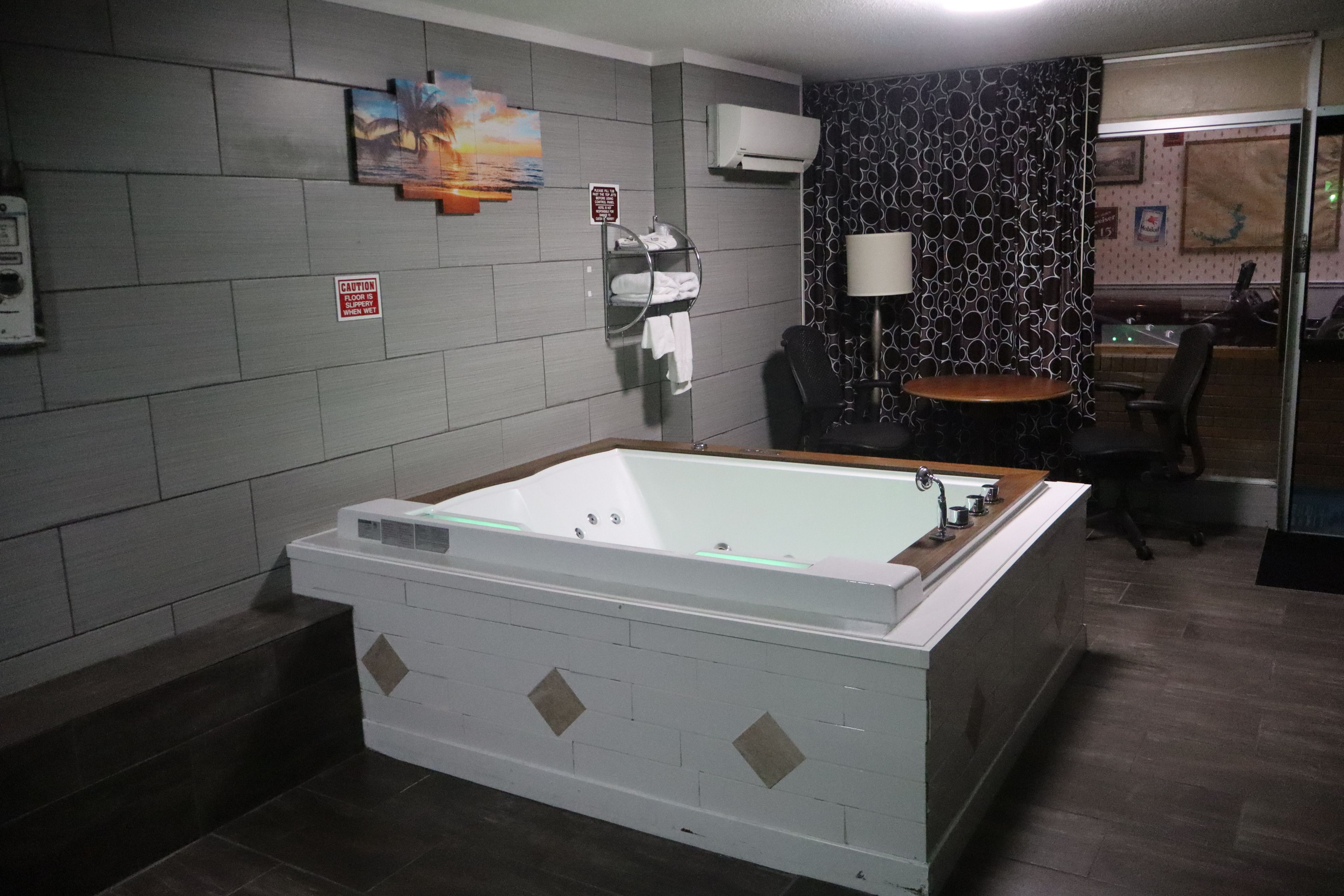 A bathroom with a large bathtub, a towel rack, a caution sign, and a wall-mounted air conditioner.
