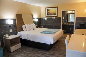 Una habitación de hotel con cama, mesita de noche y baño con espejo y lavamanos.