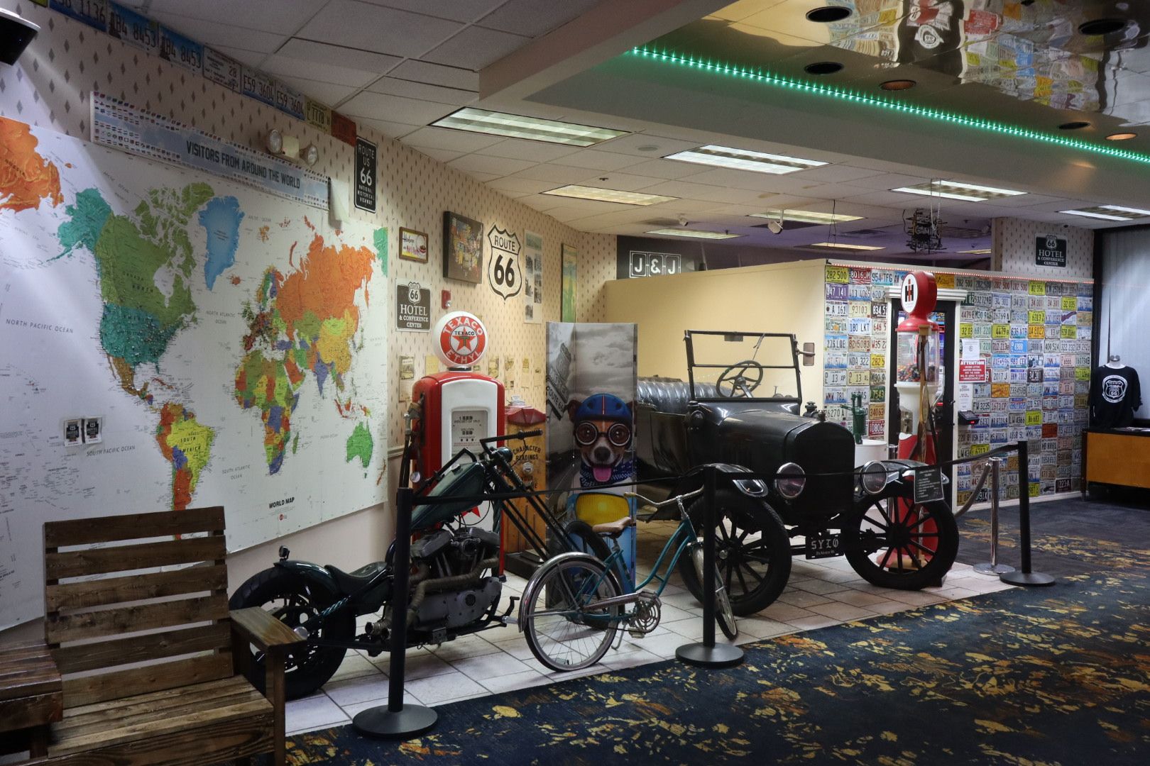 A vintage-themed exhibit with a world map, Route 66 sign, a vintage car, and a motorcycle.