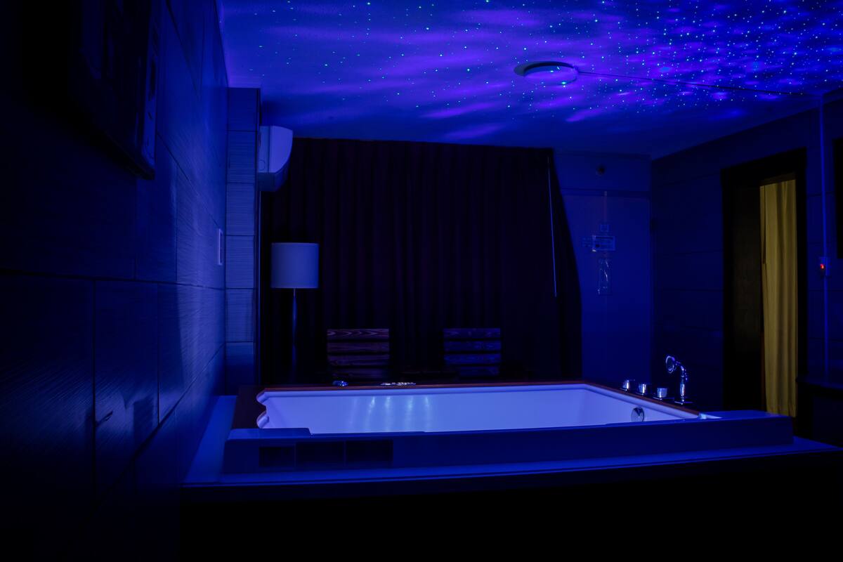 A modern bathroom with a large bathtub, a mirror, and a ceiling that displays a starry night sky effect.