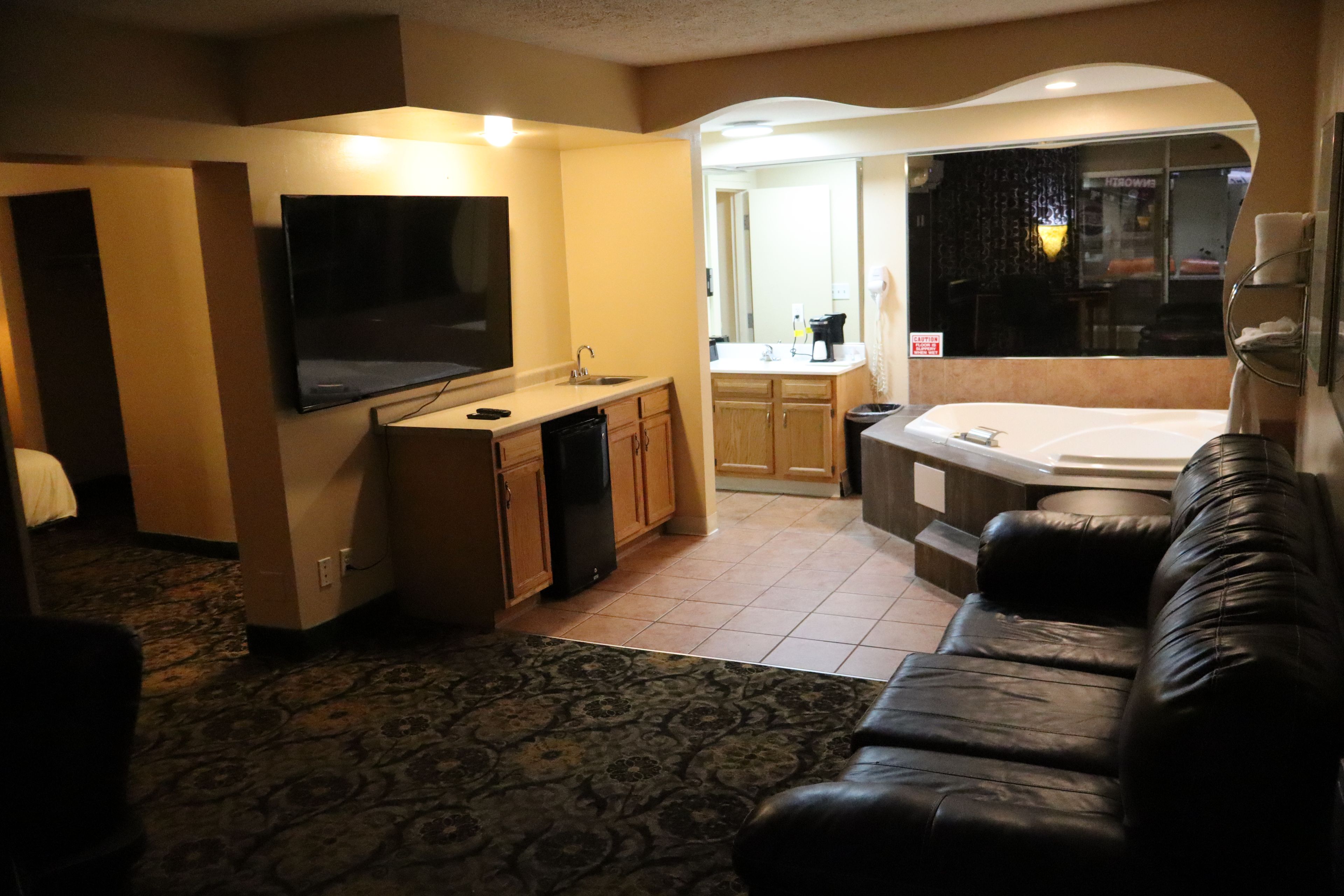 Habitación de hotel con televisión de pantalla plana, kitchenette, sofá y jacuzzi.