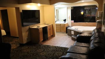 Habitación de hotel con televisión de pantalla plana, kitchenette, sofá y jacuzzi.