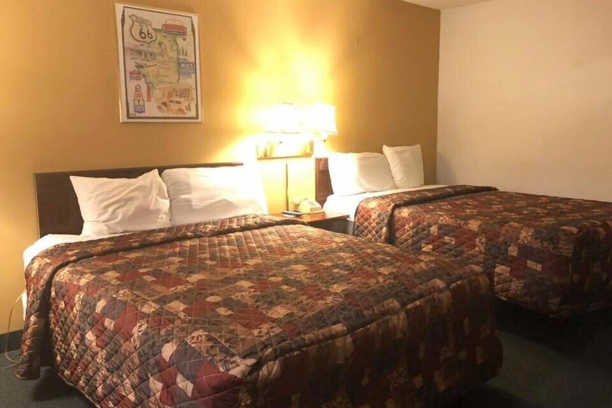 A hotel room with two beds, a nightstand, a lamp, and a wall map.