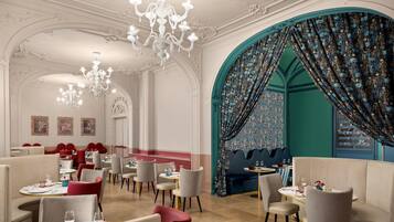 A dining area with chandeliers, red upholstered chairs, and a teal-colored wall with floral curtains.