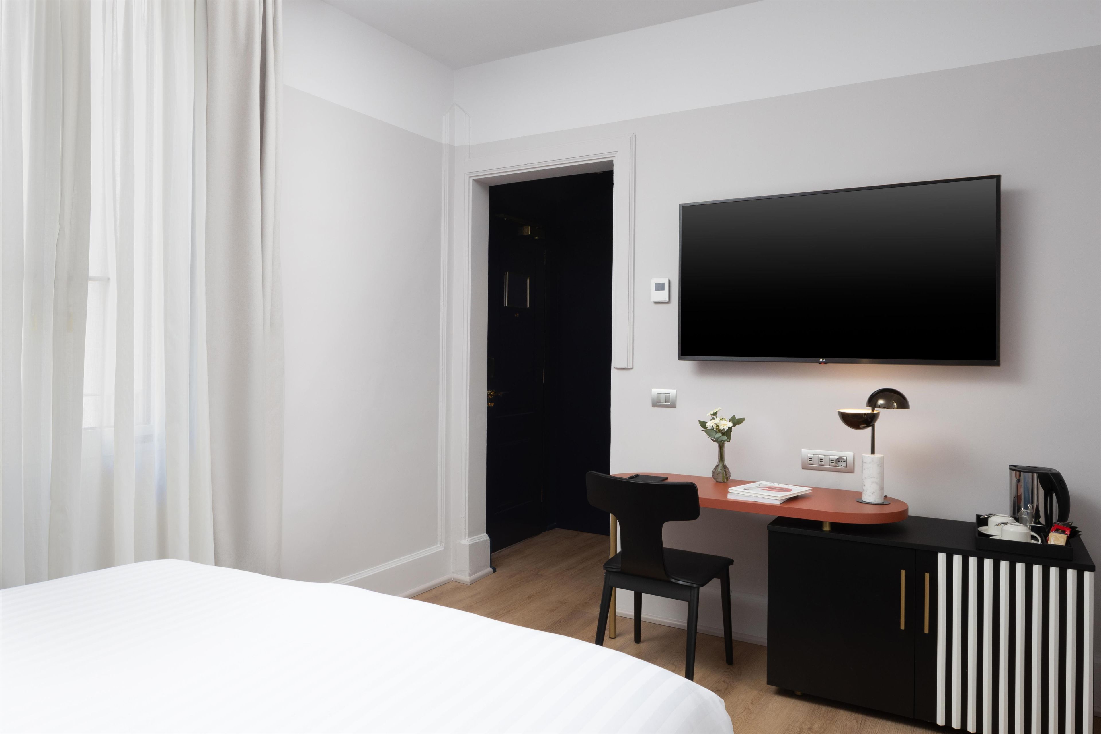 Habitación de hotel con cama, escritorio con silla, televisor de pantalla plana, cafetera y un florero con flores.
