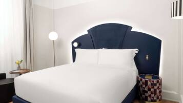Un letto rifatto con cura, con una testiera scura, una lampada da comodino e un tavolino con motivo decorativo.