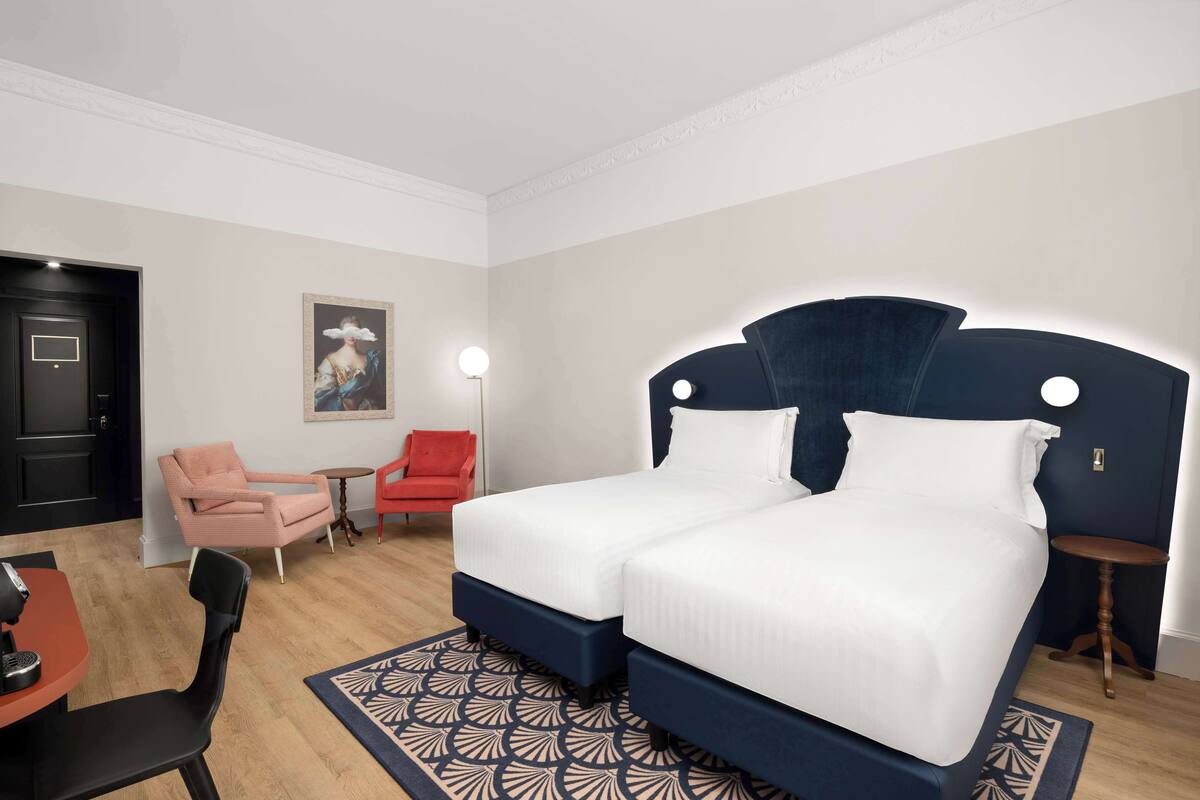Ein Hotelzimmer mit einem Doppelbett, zwei Sesseln, einem kleinen Tisch und einer Lampe.