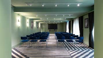 Un salón de conferencias con filas de sillas, una alfombra estampada e iluminación en el techo.