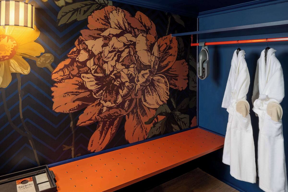 Ein Hotelzimmer mit einer großen Blumenmalerei, einer roten Bank und zwei weißen Bademänteln an einem Kleiderständer.