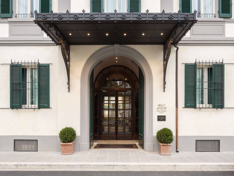 Fachada de hotel con un arco clásico, contraventanas verdes y un toldo decorativo.