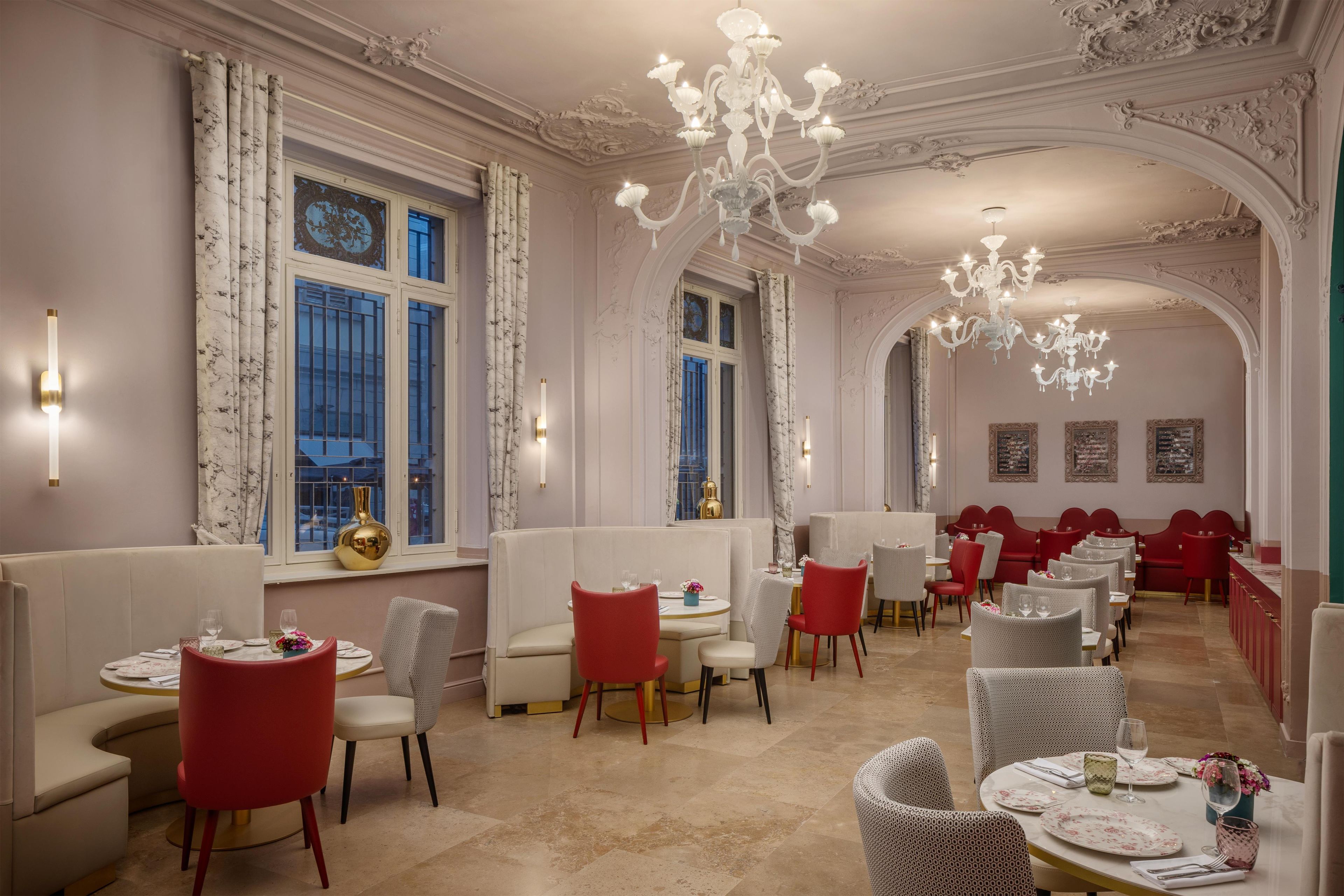 A restaurant with high ceilings, ornate chandeliers, and a mix of red and white seating.