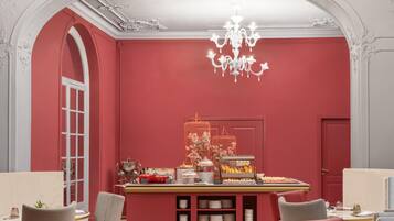 Ein Zimmer mit roter Wand, einer Kristallleuchtre, einem Vogelkäfig mit Blumen und einem Büfett.