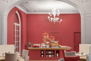 A room with a red wall, a chandelier, a birdcage with flowers, and a buffet table. - Anglo American Hotel Florence, Curio Collection by Hilton (Florence)