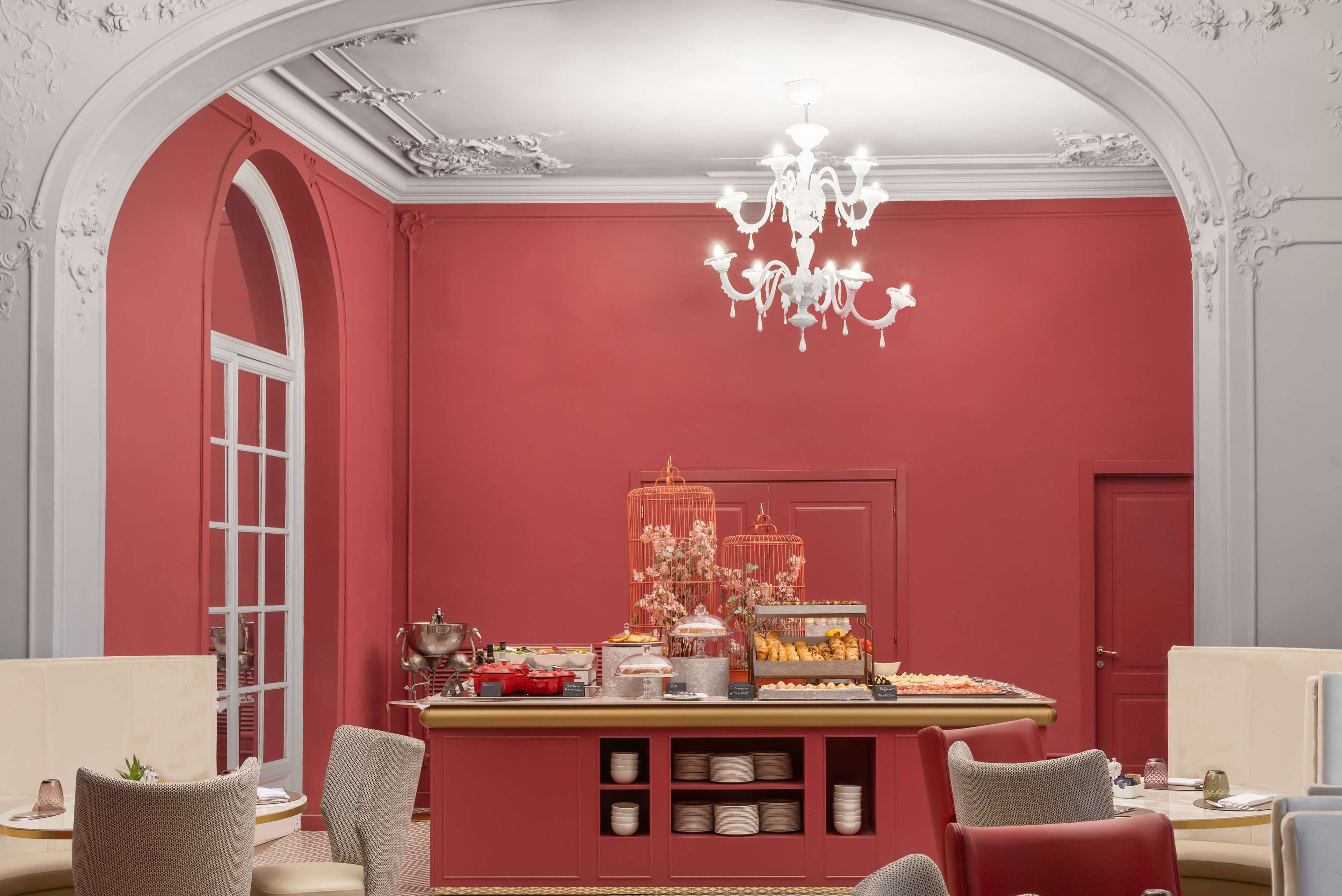 Une pièce avec un mur rouge, un lustre, une table de buffet garnie de plats et des espaces aménagés pour s’asseoir.