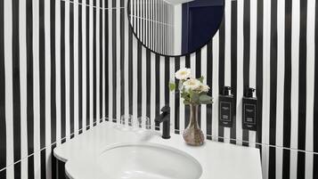 A bathroom with a white sink, black and white striped wallpaper, a round mirror, and a vase with flowers.