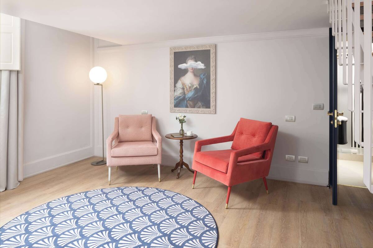 Ein Zimmer mit einem rundem Teppich, zwei Stühlen, einer Stehlampe, einem gerahmten Gemälde und einem kleinen Tisch mit einer Vase.