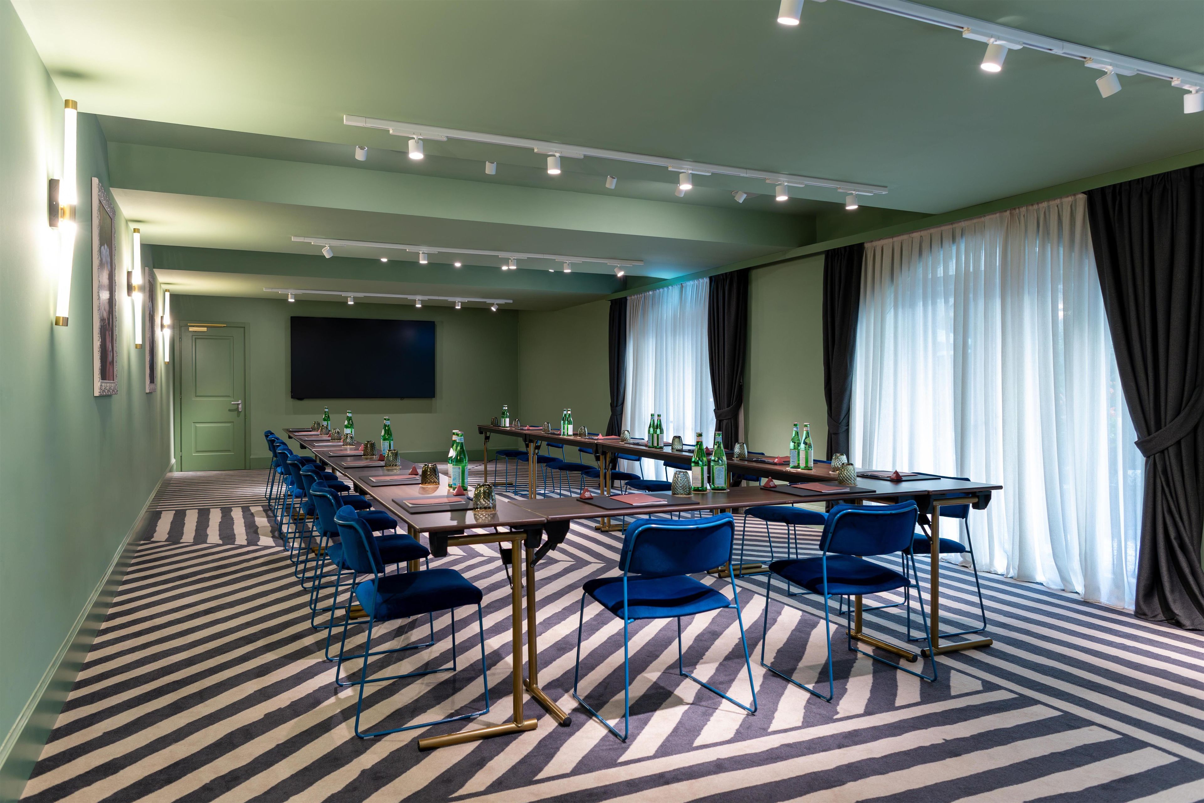 Une salle de conférence avec une longue table, des chaises bleues et un écran de projection.